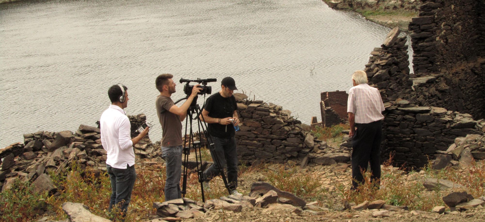 Film crew shooting beside a reservoir among stone ruins